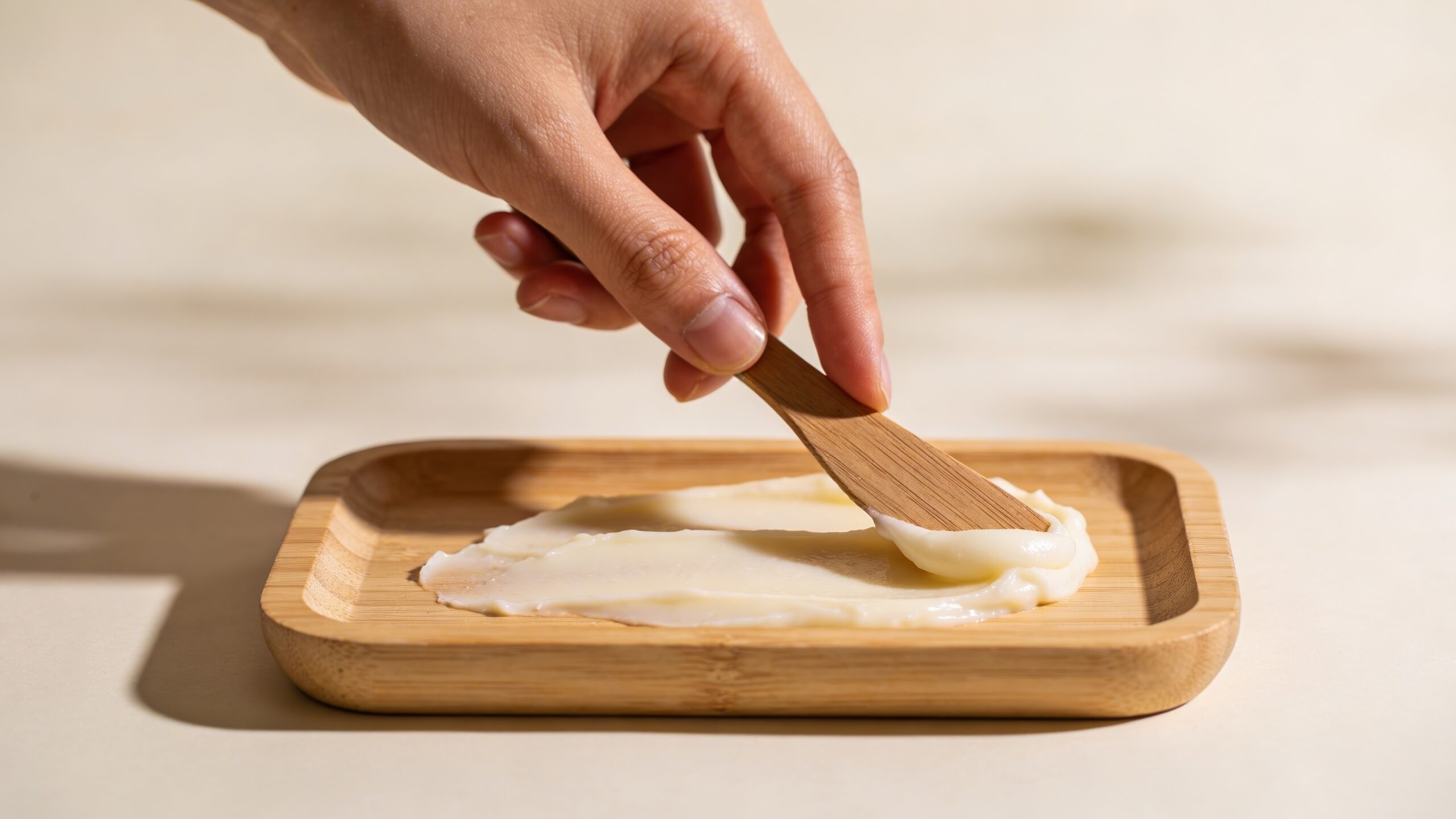 Close-up of hand spreading creamy tallow balm on minimalist wood tray with natural light Close-up of hand spreading creamy tallow balm on minimalist wood tray with natural light