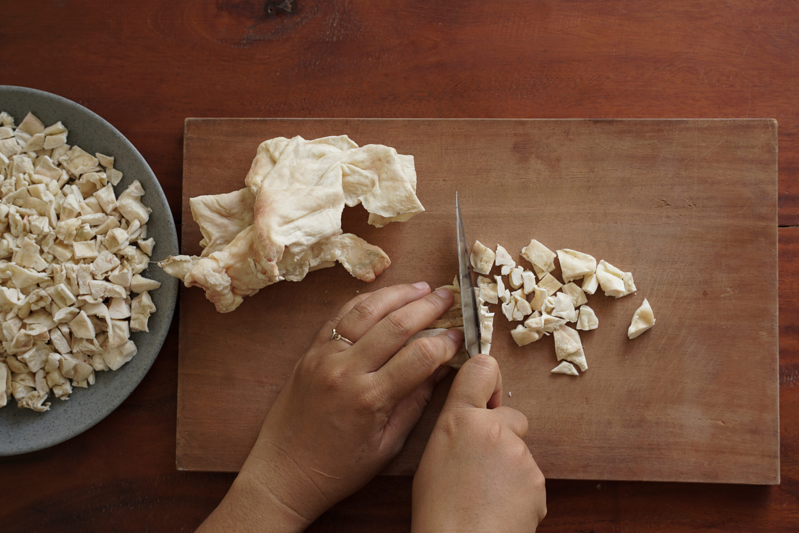Overhead view of female hand cutting raw beef fat on wooden cutting board, food preparation for homemade tallow rendering