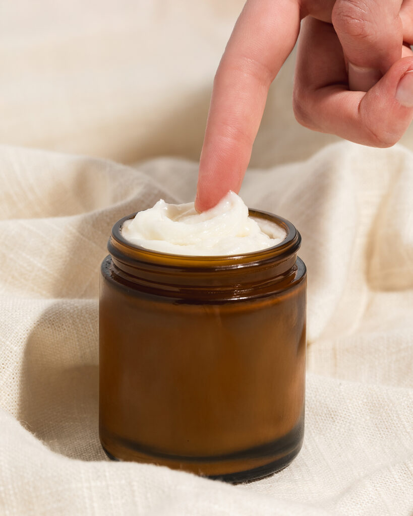 Woman's finger reaching for whipped beef tallow moisturizer in amber glass jar Woman's finger reaching for whipped beef tallow moisturizer in amber glass jar